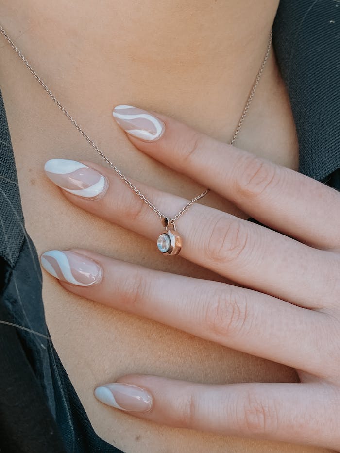 Close-up of manicured nails with artistic design holding a delicate pendant necklace.